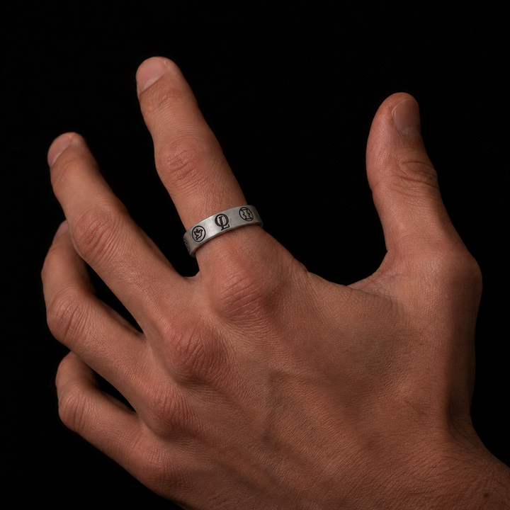 A silver band ring with engraved circular symbols, worn on the ring finger of a hand against a solid black background.