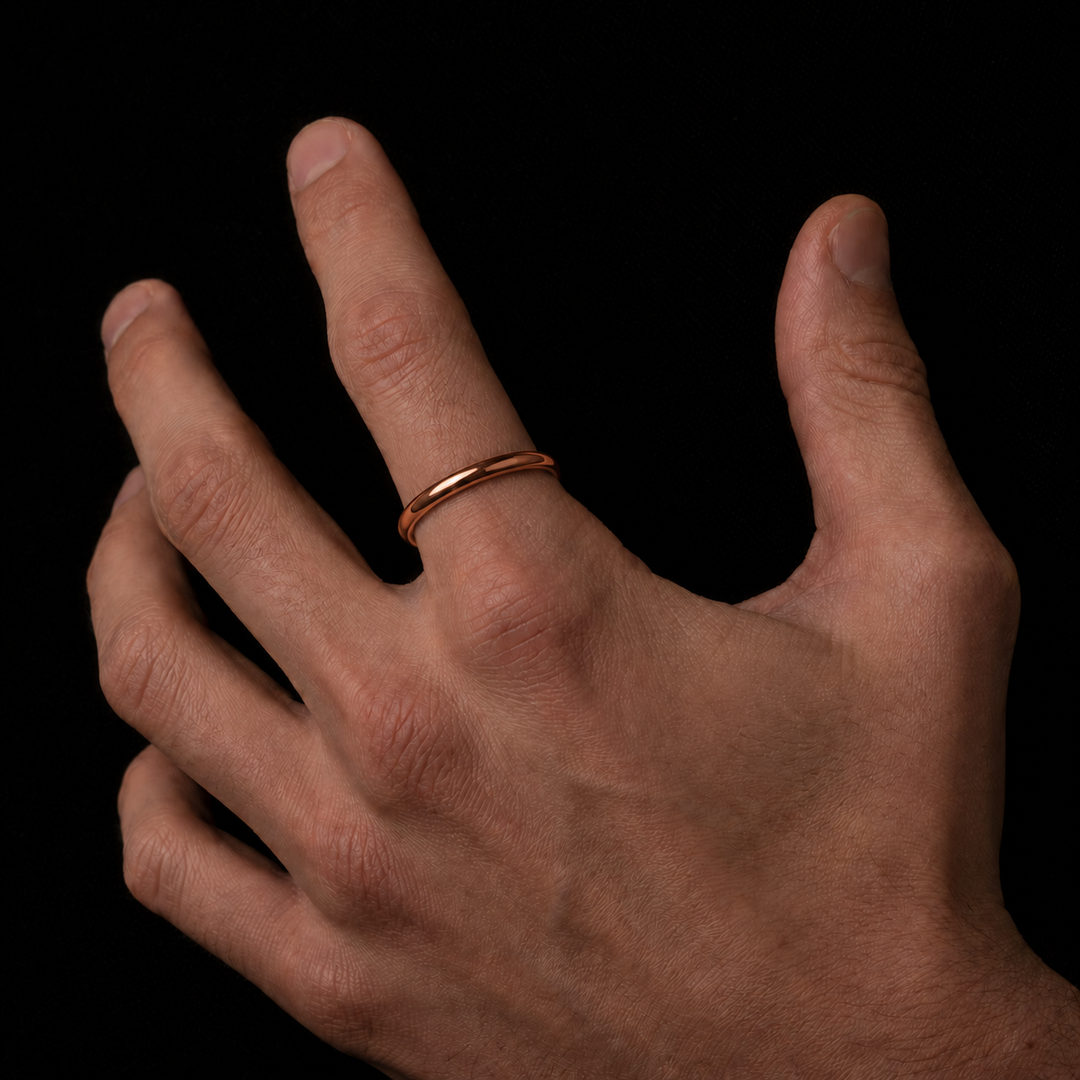 A minimalist rose gold band ring worn on the ring finger of a hand, shown against a solid black background.