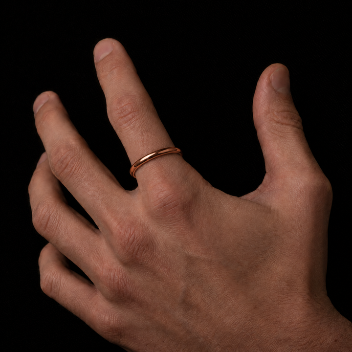 A minimalist rose gold band ring worn on the ring finger of a hand, shown against a solid black background.