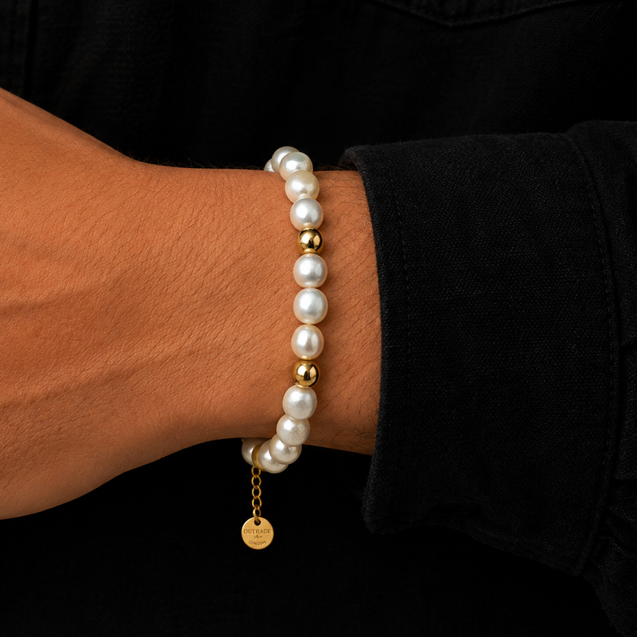 A close-up of a person's wrist wearing two stacked bracelets: one strand of white freshwater pearls with gold spacer beads, and another pearl bracelet with a small gold disc charm engraved with 'LOVE YOURSELF'.