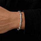 A silver-toned barbed wire bracelet worn on a person's wrist, shown against a black shirt background.