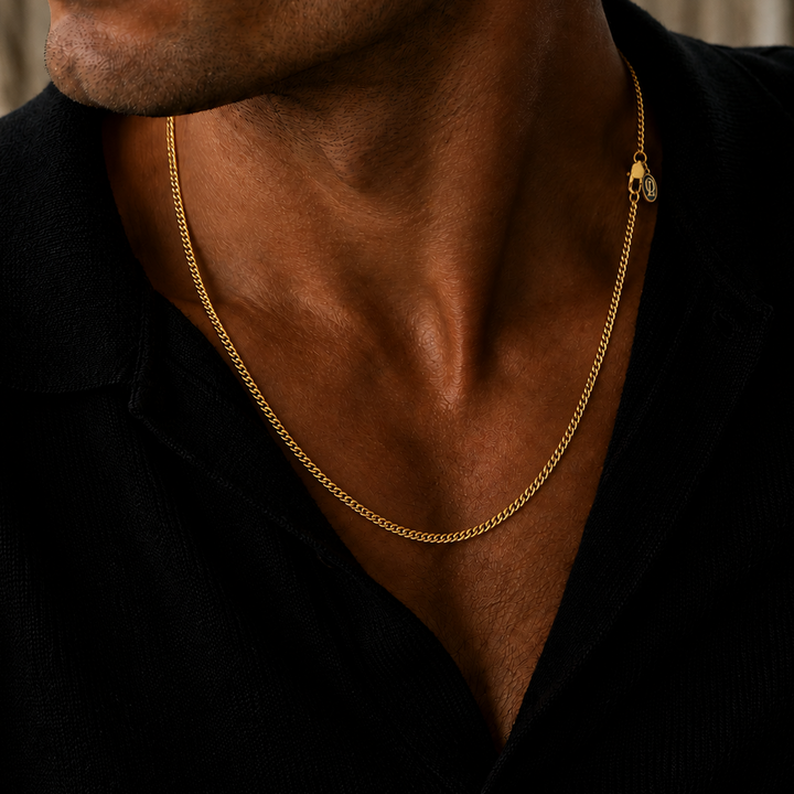 A close-up of a man's neck and chest wearing a polished yellow gold chain necklace with a small circular charm, paired with a black collared shirt.