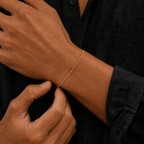 A close-up of a person wearing a delicate gold chain bracelet on their wrist, wearing a black textured shirt.