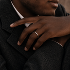 A close-up of a man's hand resting on his lapel, wearing a simple, polished silver band ring.