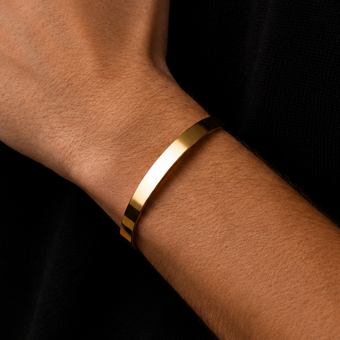 A slim, polished gold metal cuff bracelet worn on a person's wrist, shown against a dark black knit sweater.
