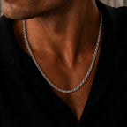 Close-up lifestyle image of a men’s polished silver wheat chain necklace, featuring a tightly woven interlocking link design worn around the neck with an open black collared shirt for a refined, understated luxury look