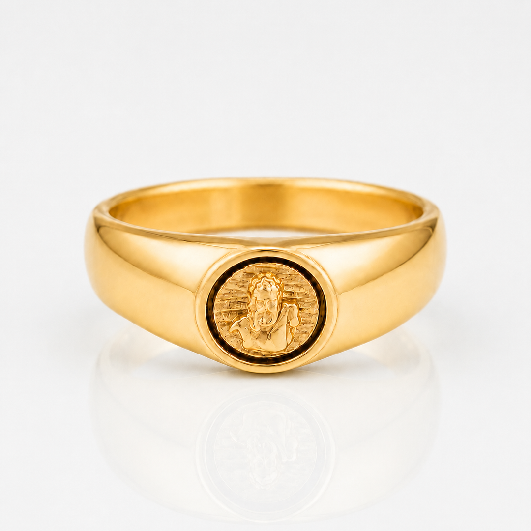 A polished yellow gold signet ring featuring an oval face with an embossed figure, photographed on a clean white reflective surface.