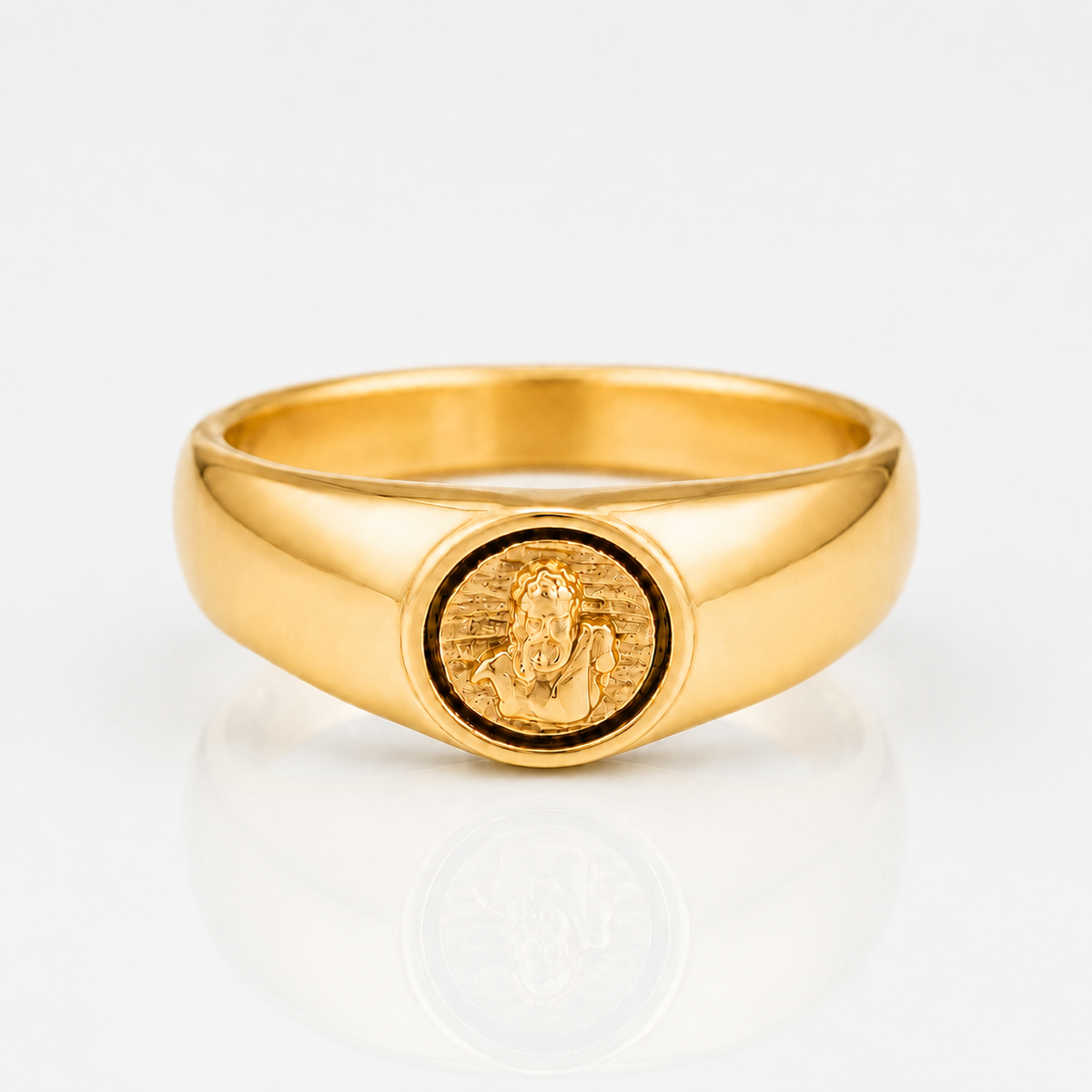 A polished yellow gold signet ring featuring an oval face with an embossed figure, photographed on a clean white reflective surface.