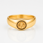 A polished yellow gold signet ring featuring an oval face with an embossed figure, photographed on a clean white reflective surface.