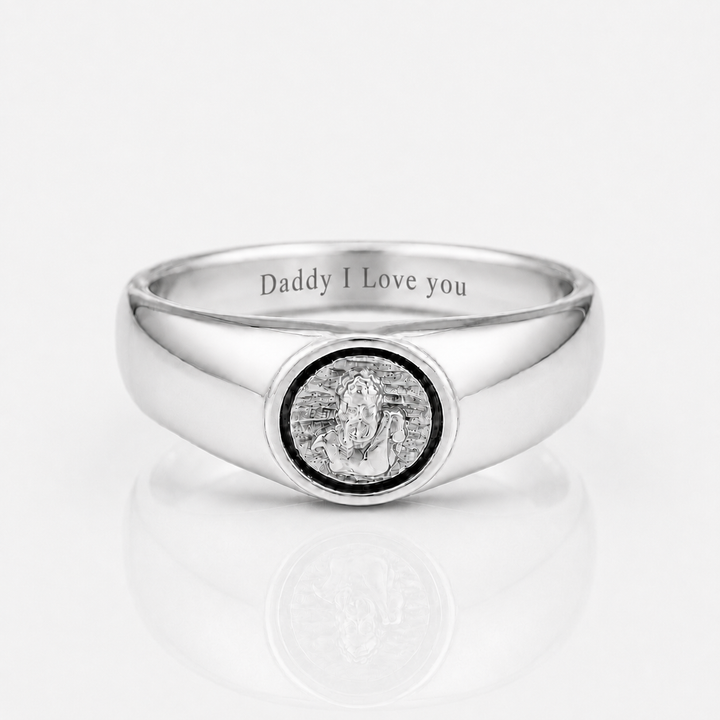 A polished silver signet ring engraved with 'Daddy I Love you' on the inside band, featuring a circular medallion with a silver statue of Lord Ganesha in the center, set against a clean white background with a soft reflection.