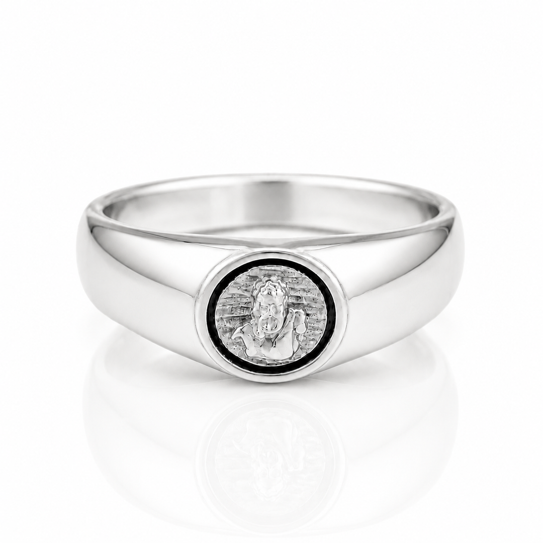 A polished silver signet ring featuring a circular medallion with a religious figure, set against a clean white background with a soft reflection.