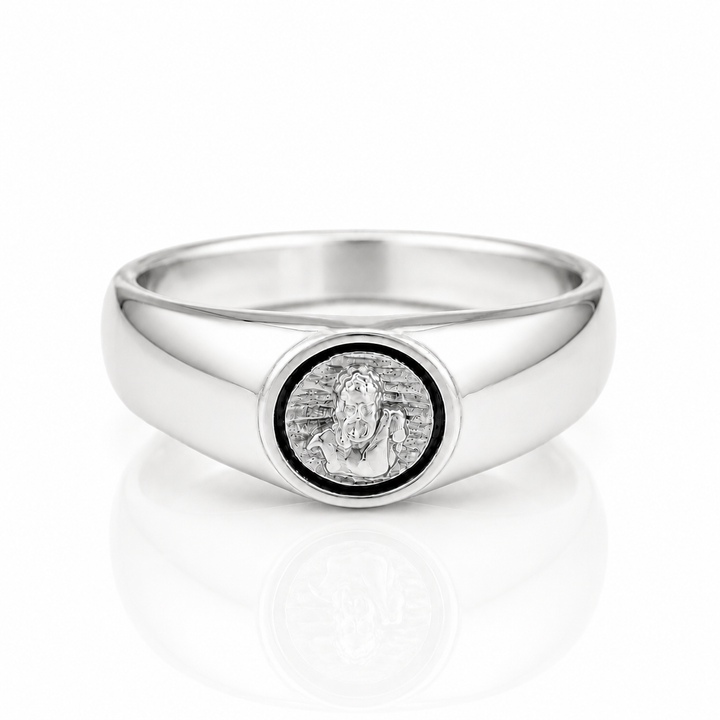 A polished silver signet ring featuring a circular medallion with a religious figure, set against a clean white background with a soft reflection.