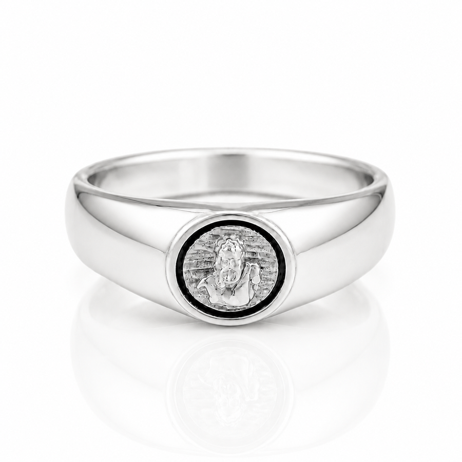 A polished silver signet ring featuring a circular medallion with a religious figure, set against a clean white background with a soft reflection.