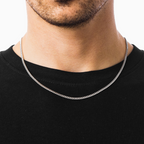 Silver chain necklace worn by a person on a plain background