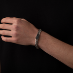 Hand wearing a silver chain bracelet on a black background