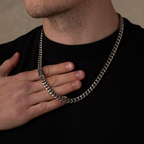 Man wearing a silver chain necklace against a neutral background with hand holding chain