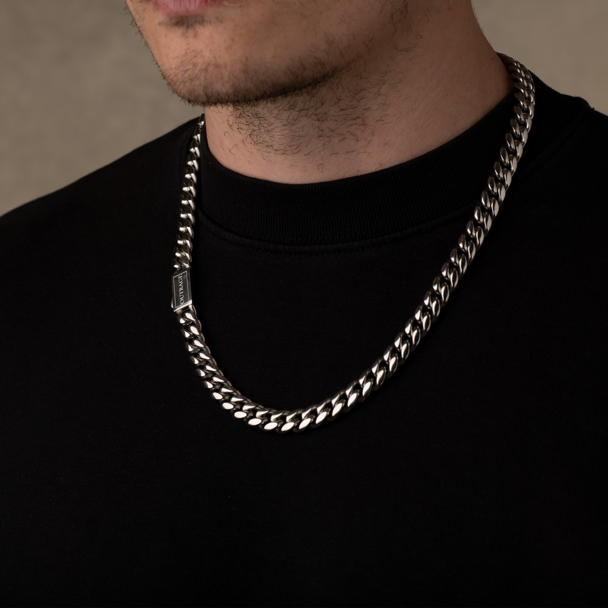 Man wearing a silver chain necklace against a neutral background