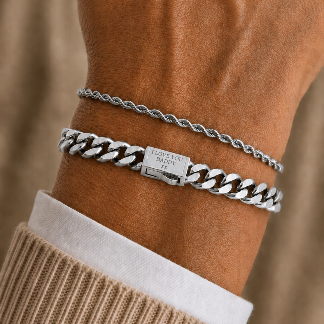 Two silver bracelets worn on a person's wrist, including a thin chain bracelet and a chunky curb-link bracelet with a clasp engraved with 'JACKSON HOLE'.