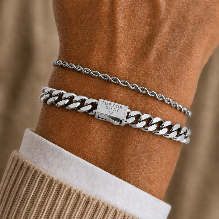 Two silver bracelets worn on a person's wrist, including a thin chain bracelet and a chunky curb-link bracelet with a clasp engraved with 'JACKSON HOLE'.