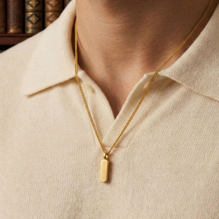 A gold necklace with a rectangular pendant is worn around a person's neck.