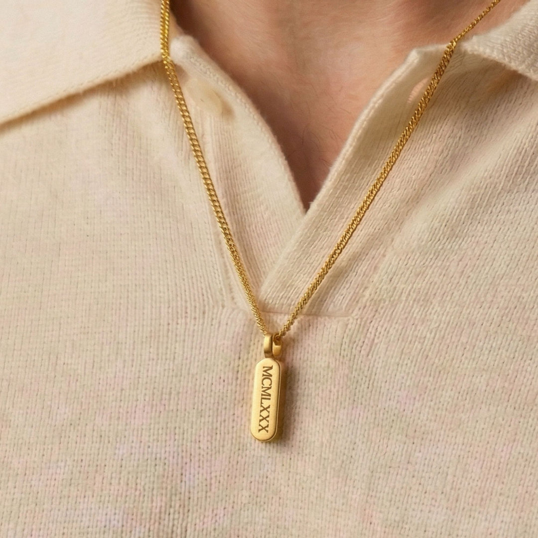 A gold necklace with a rectangular pendant is worn around a person's neck.