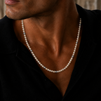 A close-up of a man wearing a classic pearl necklace with silver spacer beads, styled with a black shirt.