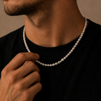 A close-up lifestyle shot of a man wearing a classic white pearl necklace with a black t-shirt, adjusting the necklace with his hand against a warm, neutral background.