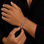 A close-up of a person's wrist wearing a silver barbed wire bracelet, with their fingers adjusting the clasp. The person is wearing a black button-down shirt.