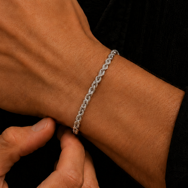 A close-up of a person's wrist wearing a silver-toned twisted chain bracelet, with their other hand adjusting it. They are wearing a black button-down shirt.