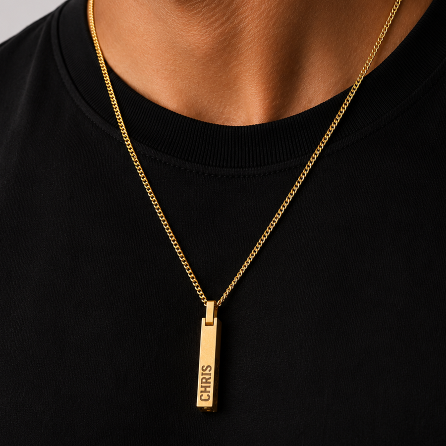 A gold-toned nameplate necklace with a vertical bar pendant engraved with the name 'CHRIS', worn by a person wearing a black crewneck shirt.